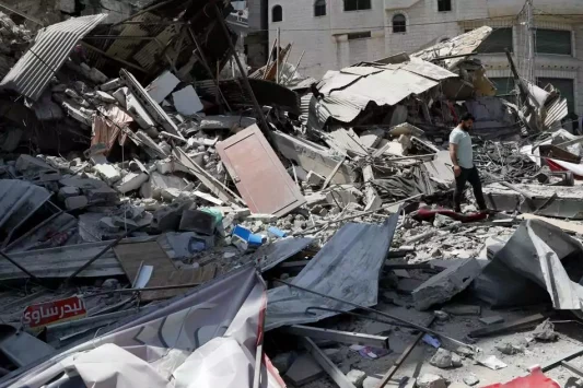 Seorang pria memeriksa puing puing bangunan pemukiman yang hancur akibat serangan udara Israel, di Kota Gaza, Kamis, 20 Mei 2021. (AP Photo / Adel Hana)