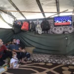 Wael al-Nabahin dan keluarganya menonton televisi dalam tenda di lokasi pengungsian Deir el-Balah, kawasan Gaza Tengah. @Al Jazeera